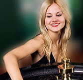 A croupier at a casino table looking towards it and with her right arm on the cylinder as if she were going to spin it.