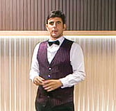 A dealer dressed in a white shirt, purple vest and black bow tie talking to the camera.