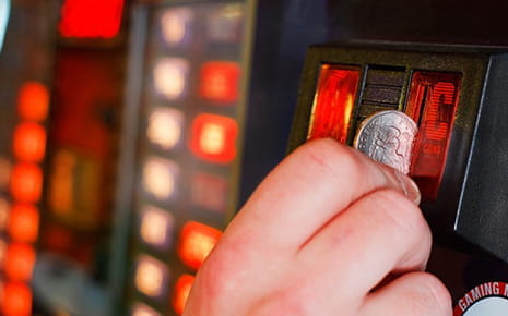 A hand inserts a coin into a slot machine.